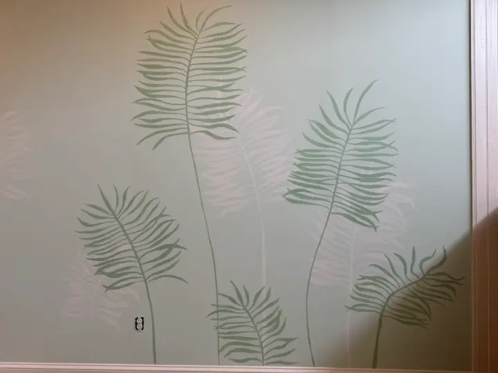 Detail of overlapping sage and white fern fronds painted on an interior wall