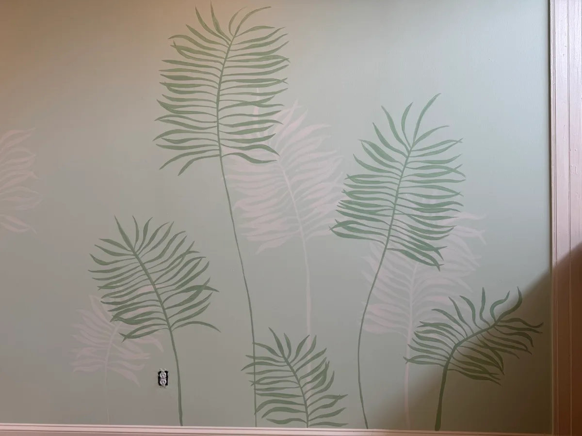 Detail of overlapping sage and white fern fronds painted on an interior wall
