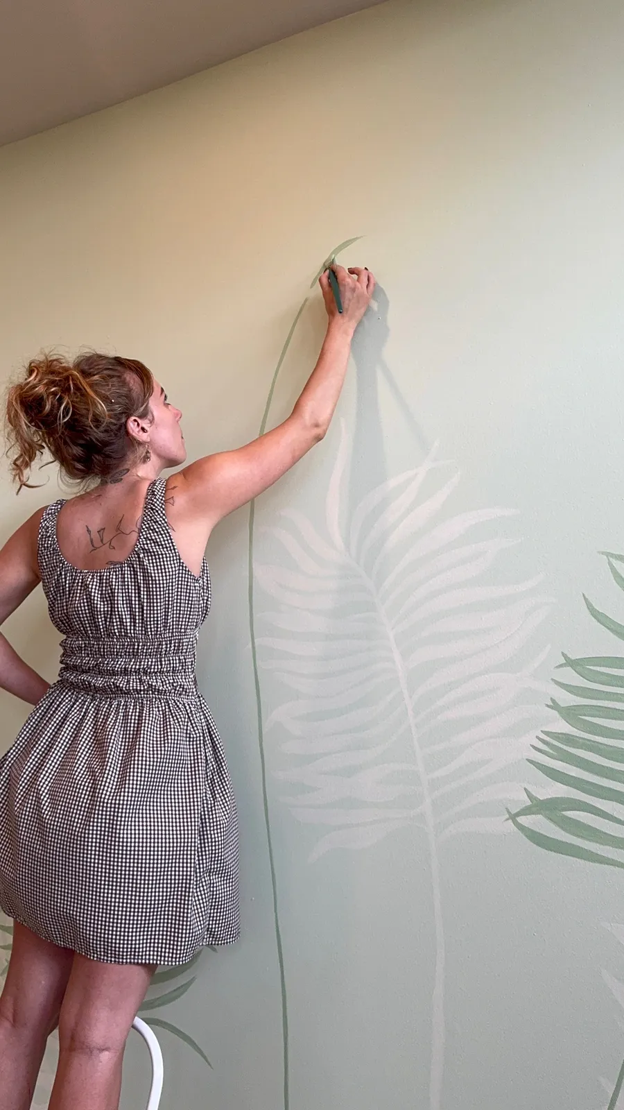Artist Shannon Hope McAnney hand painting a tall fern mural indoors