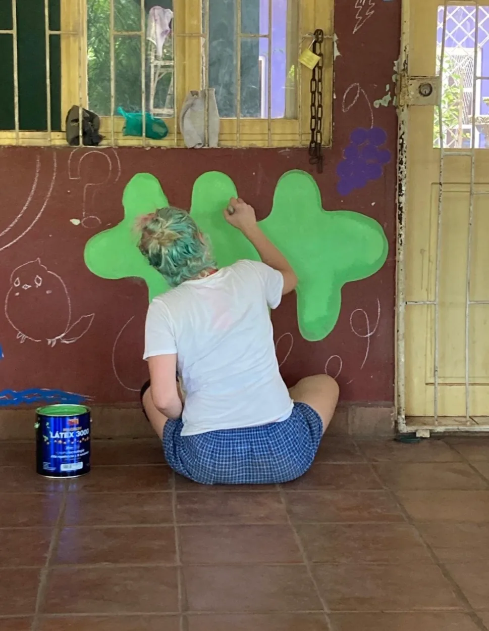 Artist Shannon Hope McAnney painting a bright green shape on a community mural wall
